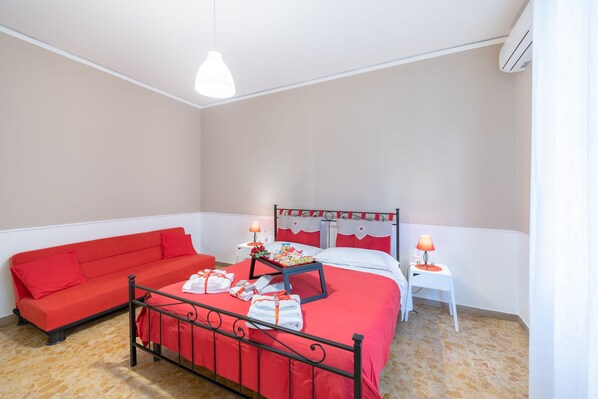 A room with a bed, a red sofa, a small table with a lamp, and an air conditioning unit. - Terrazze Italiane City Center (Verona)