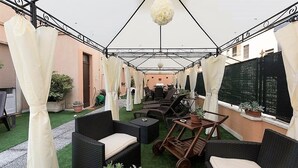 An outdoor patio area with wicker furniture, a wooden cart, and a hanging light fixture. - Terrazze Italiane City Center (Verona)