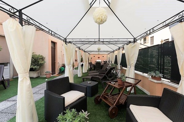 Un patio al aire libre con mobiliario de mimbre, un carro de madera y una lámpara colgante.