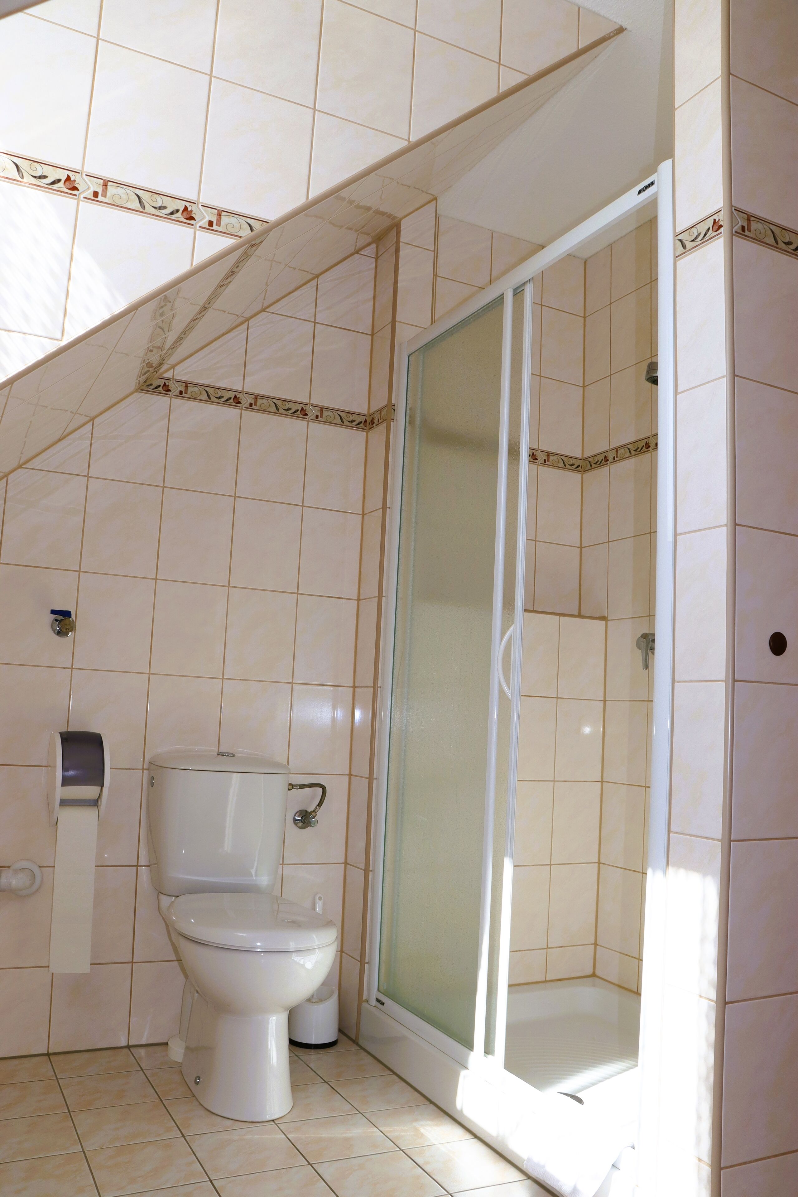 A bathroom with a toilet, a glass shower enclosure, and tiled walls.