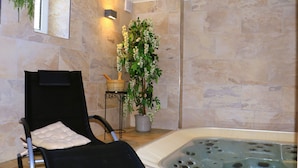 Une salle de spa avec un fauteuil noir, un jacuzzi, une plante en pot et un mur en pierre.