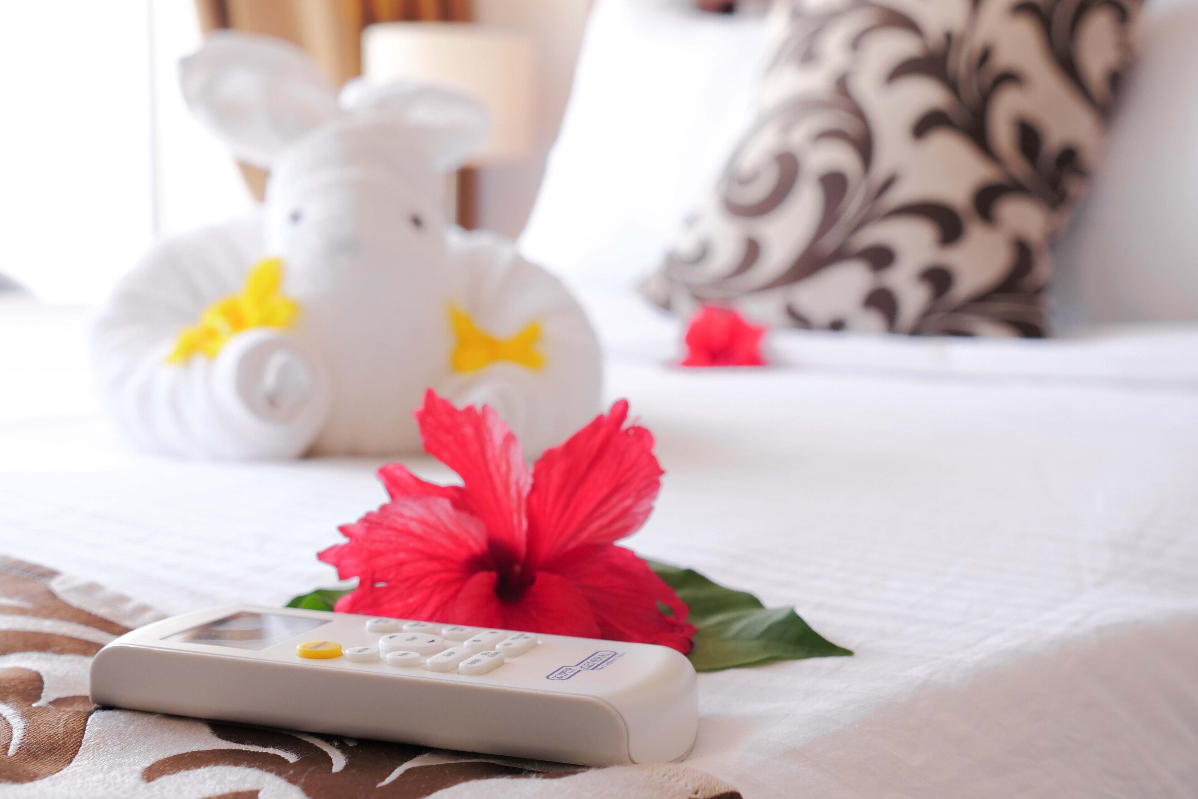A bed with a remote control, a white elephant-shaped object, and a red hibiscus flower.