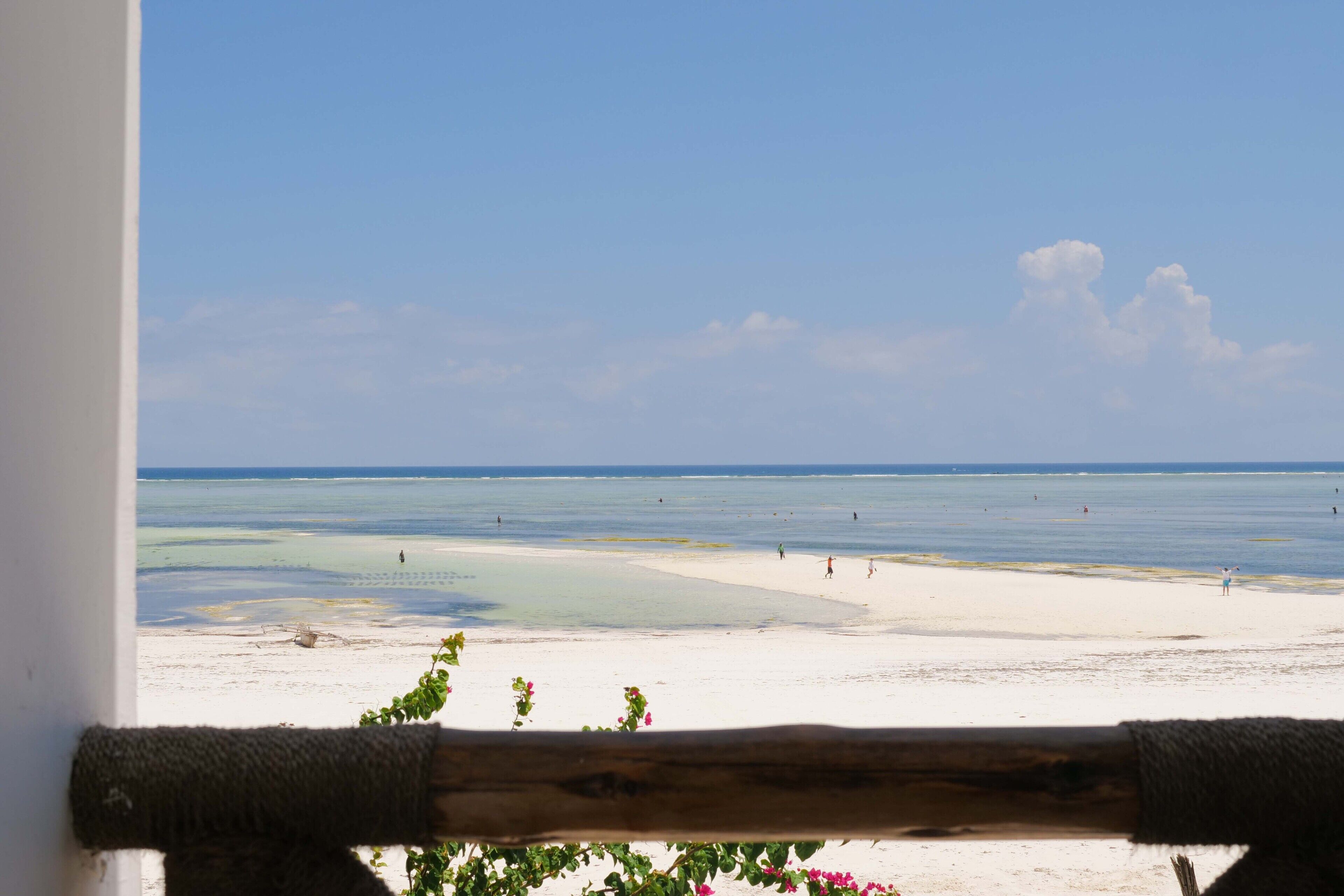 A beach view with a wooden railing, clear sky, and calm sea.