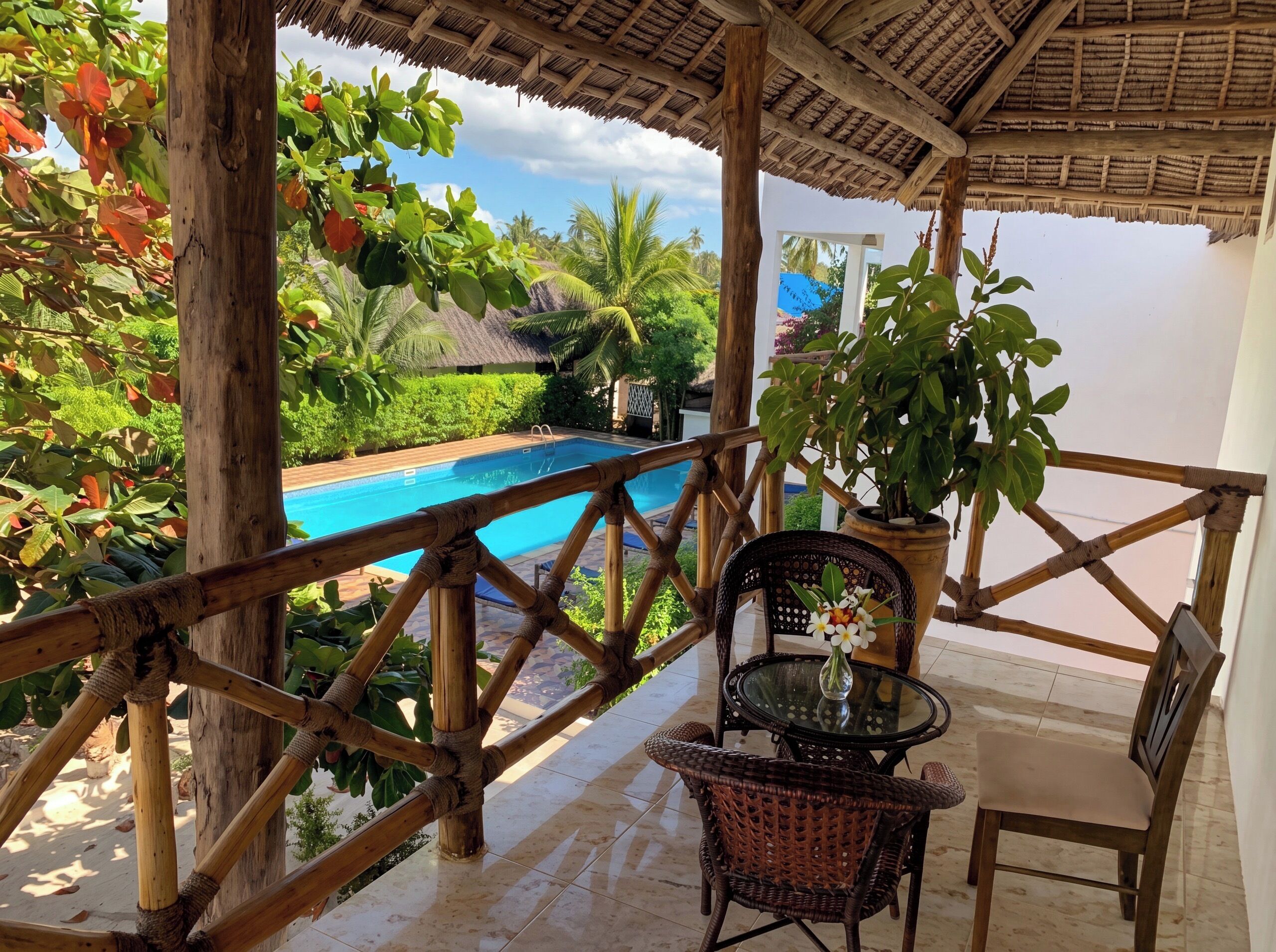 A covered outdoor area with a pool, wooden railing, and wicker furniture.