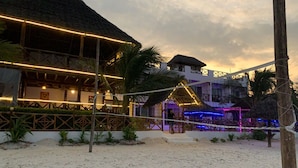 Un resort sulla spiaggia con un edificio a tetto di paglia, una recinzione in legno e una spiaggia sabbiosa.