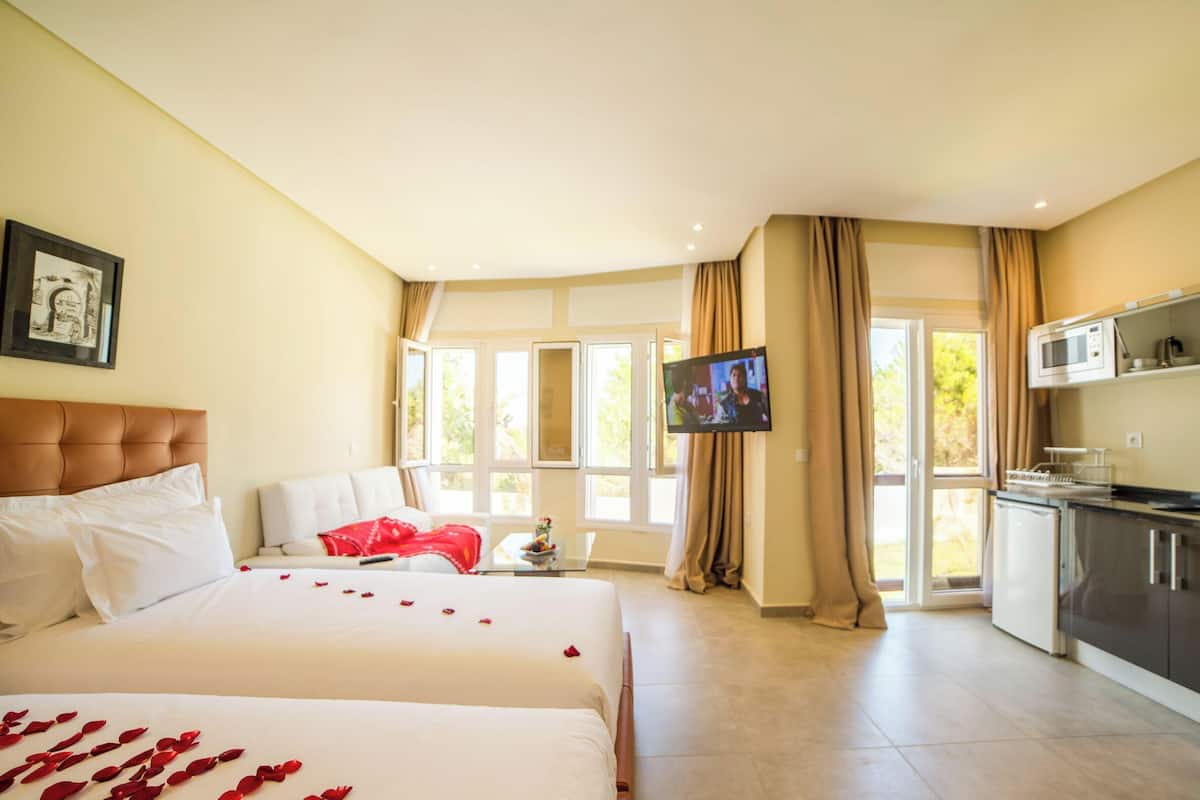 Ein Hotelzimmer mit Bett, einer Sitzecke, einem Fernseher, einer Küchenzeile und großen Fenstern.