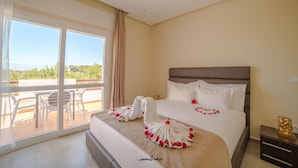 Ein Hotelzimmer mit einem großen Bett, einem Balkon mit Tisch und Stühlen und Blick auf die Landschaft.