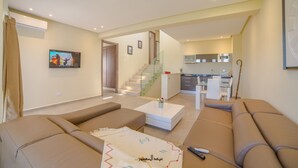Ein modernes Wohnzimmer mit einer Couch, einem Couchtisch und einem Fernseher. Eine Treppe führt zu einem Küchenbereich.