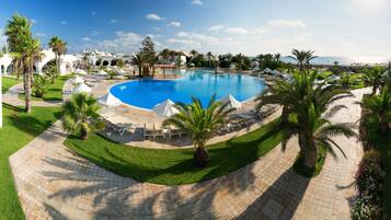 Une grande piscine entourée de palmiers et de chaises longues, avec une vue sur la mer en arrière-plan.
