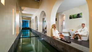 A spa area with a long pool, seating areas, and a door leading to another room. - Iliade Aqua Park Djerba (Djerba Midun)