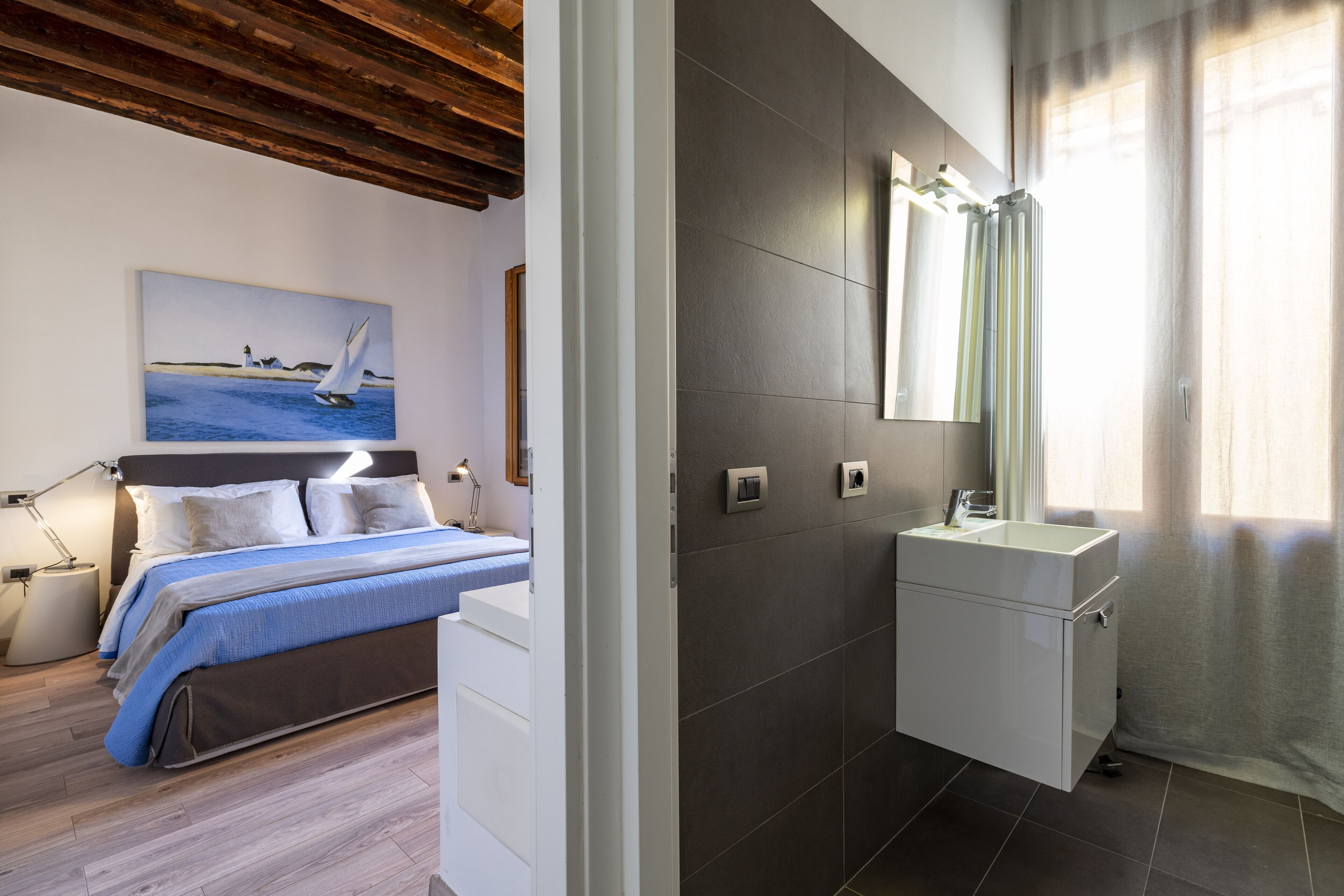 Un dormitorio con cama, mesita de noche, lámpara y un cuadro de un velero.