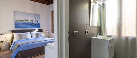 Un dormitorio con cama, mesita de noche, lámpara y un cuadro de un velero.