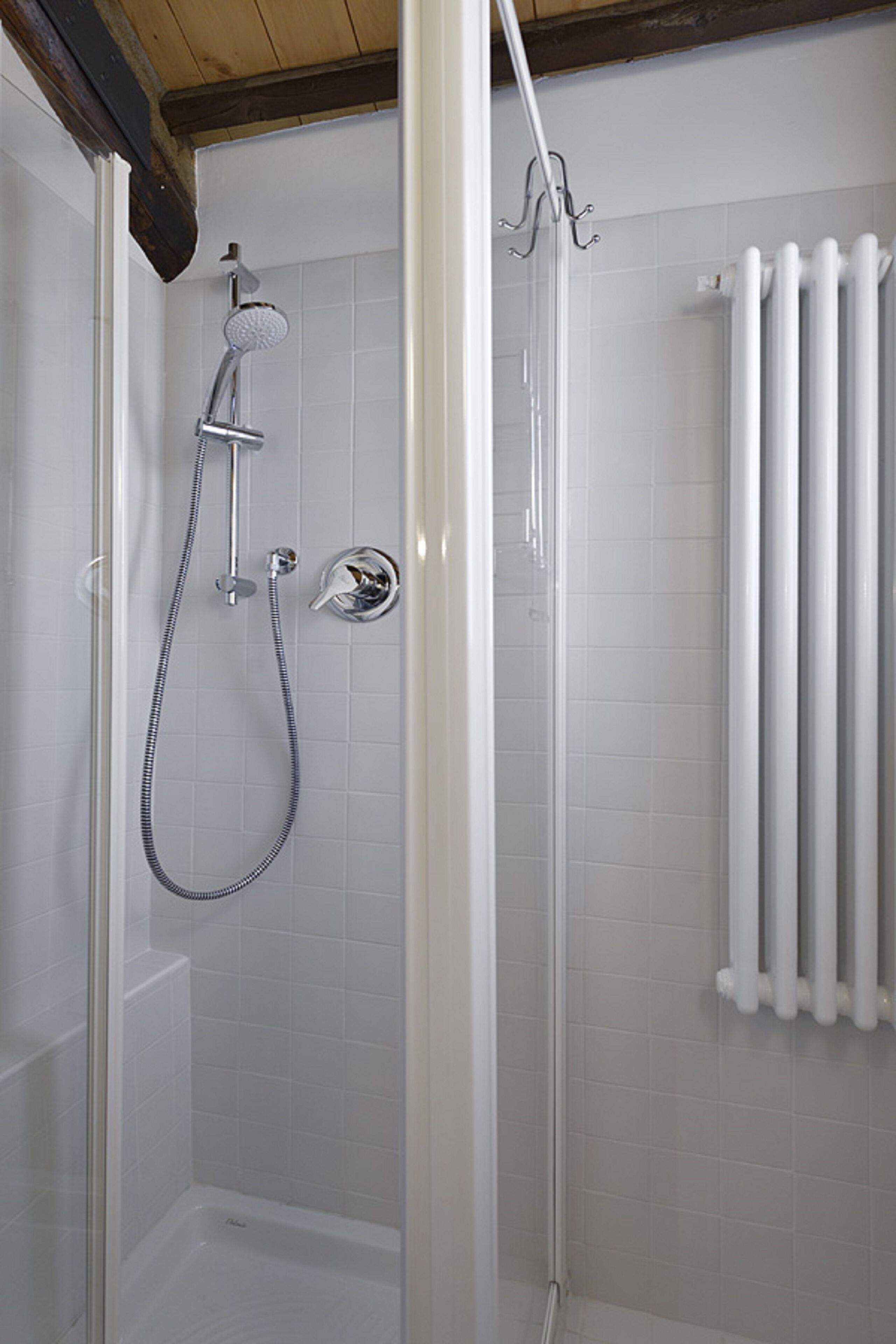 A glass-enclosed shower with a handheld showerhead and a wall-mounted faucet.