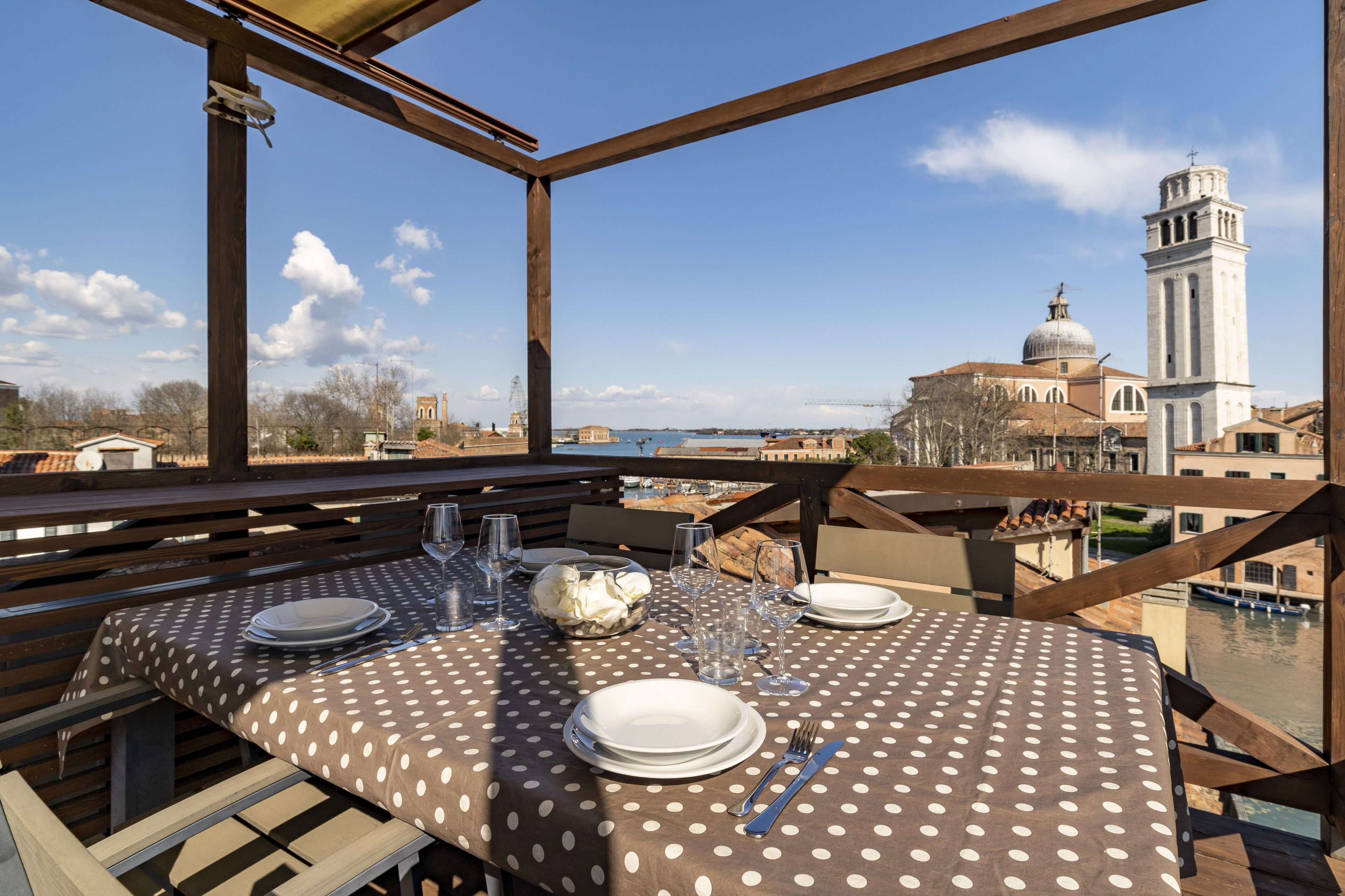 Un espace de restauration en plein air avec une nappe à pois, situé devant un ciel dégagé et un bâtiment historique doté d’un clocher.