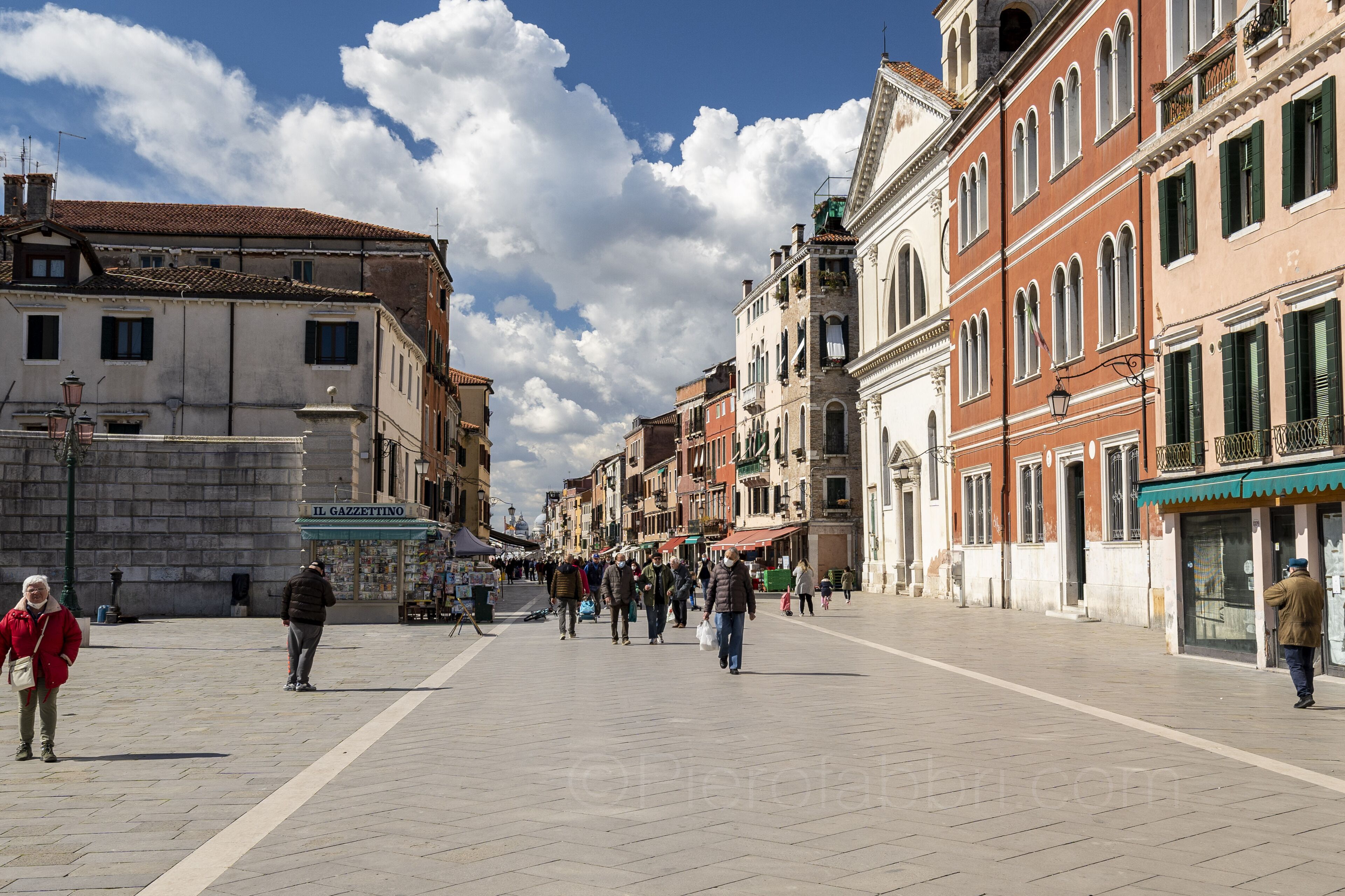 A wide pedestrian street lined with historic buildings, a clear sky, and people walking.