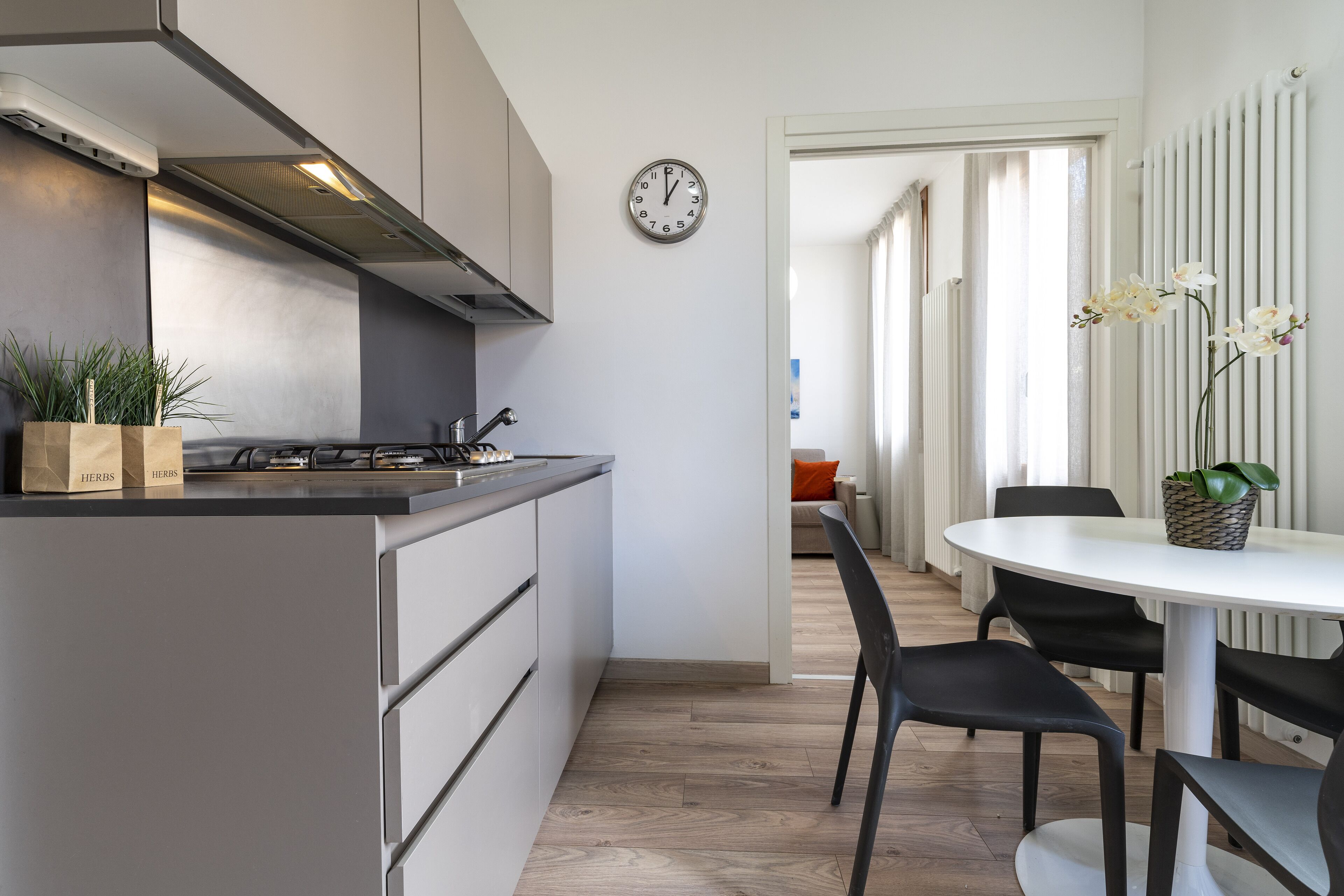 Une cuisine moderne avec un îlot central, un coin repas doté d’une table ronde et de chaises, et une horloge au mur.