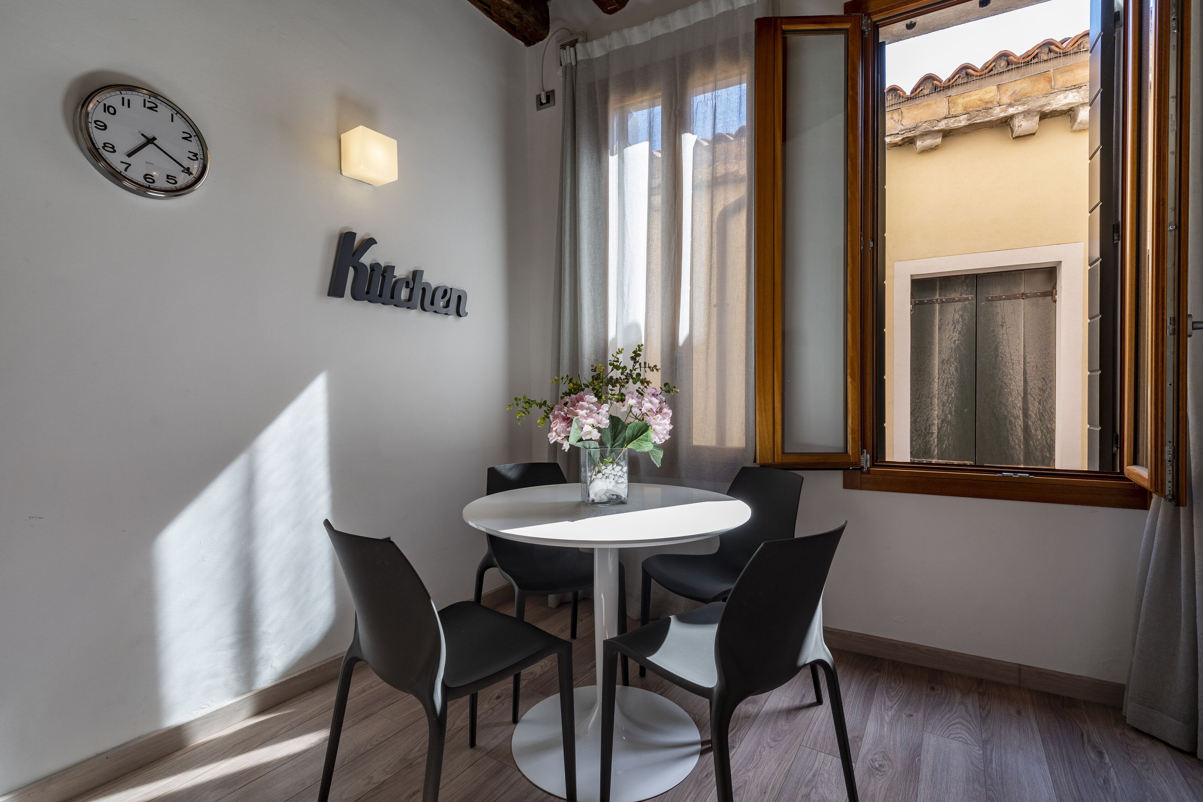 A dining area with a round table, four chairs, a clock, and a wall-mounted sign.