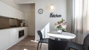 A modern kitchen with a clock, a 'Kitchen' sign, and a dining area with chairs and a table.