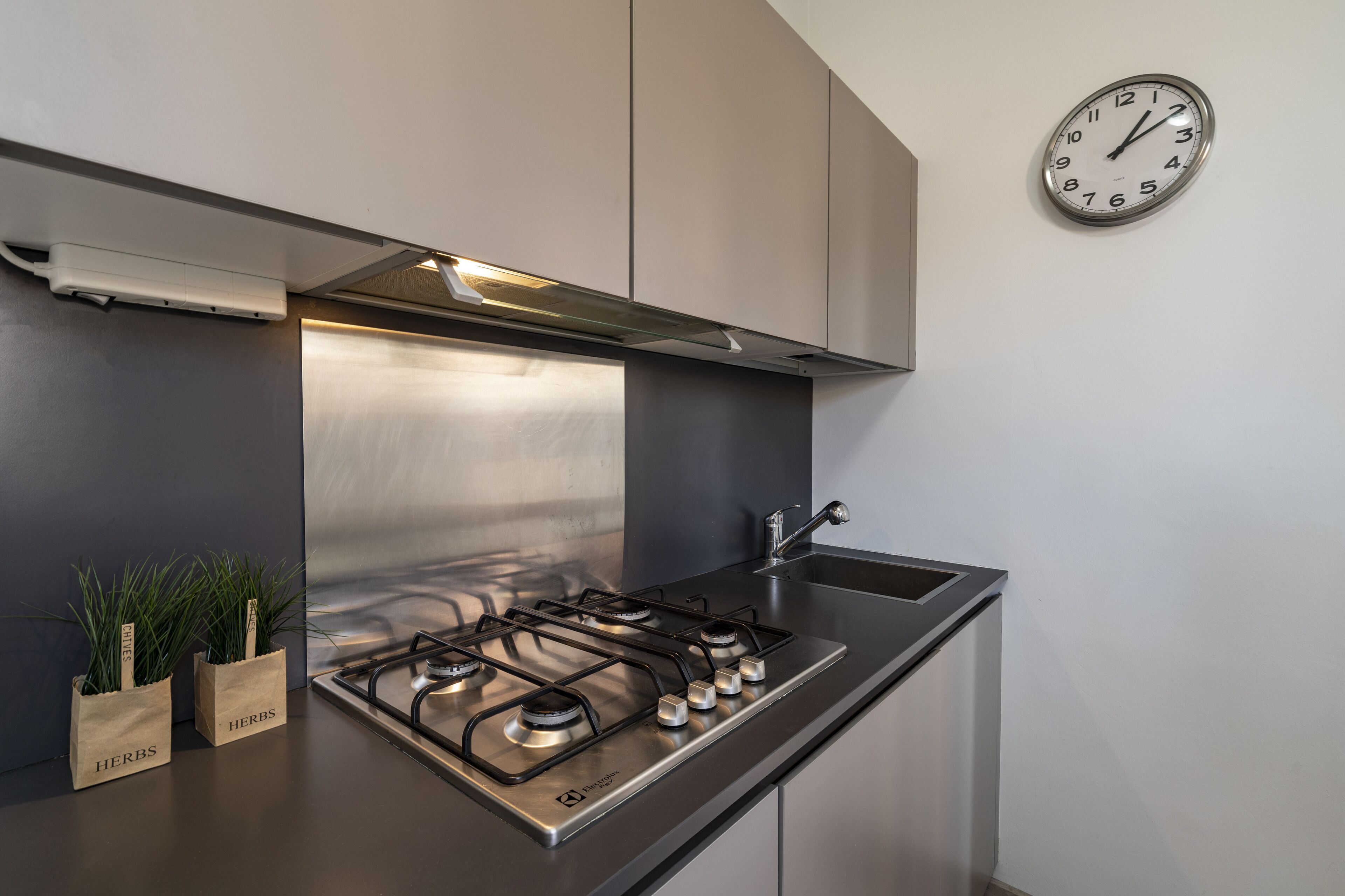 A modern kitchen with a stainless steel gas stove, a built-in oven, and a wall-mounted clock.