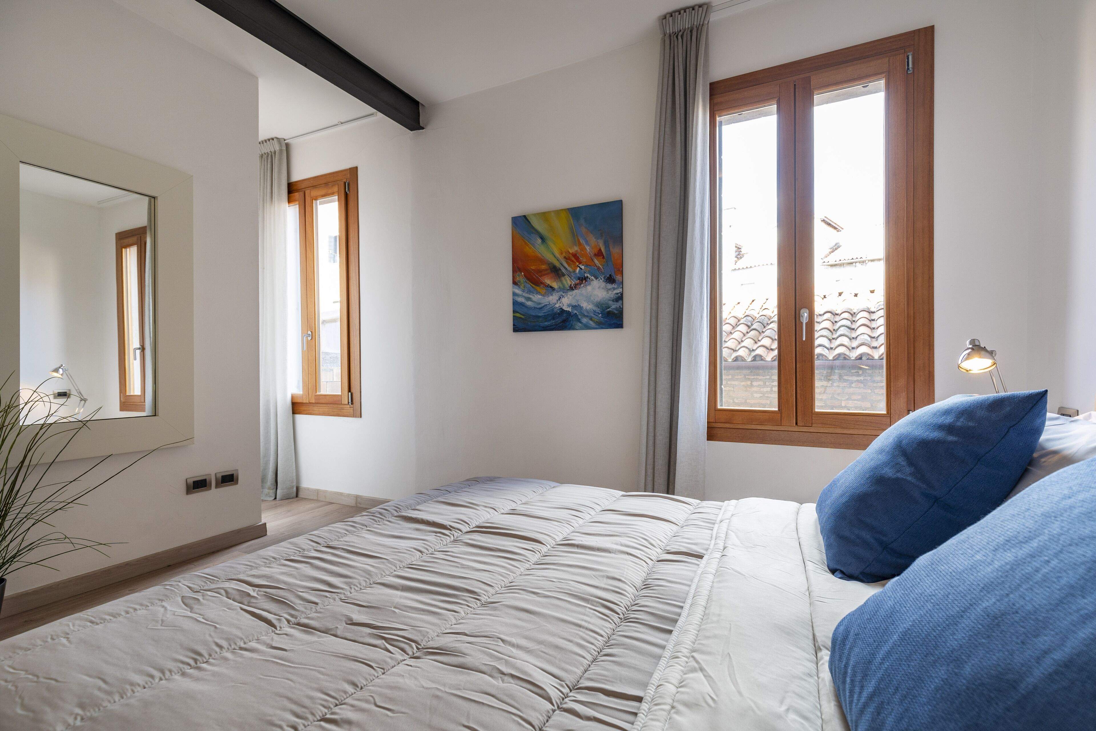 A bedroom with a large bed, a painting on the wall, and a window with curtains.
