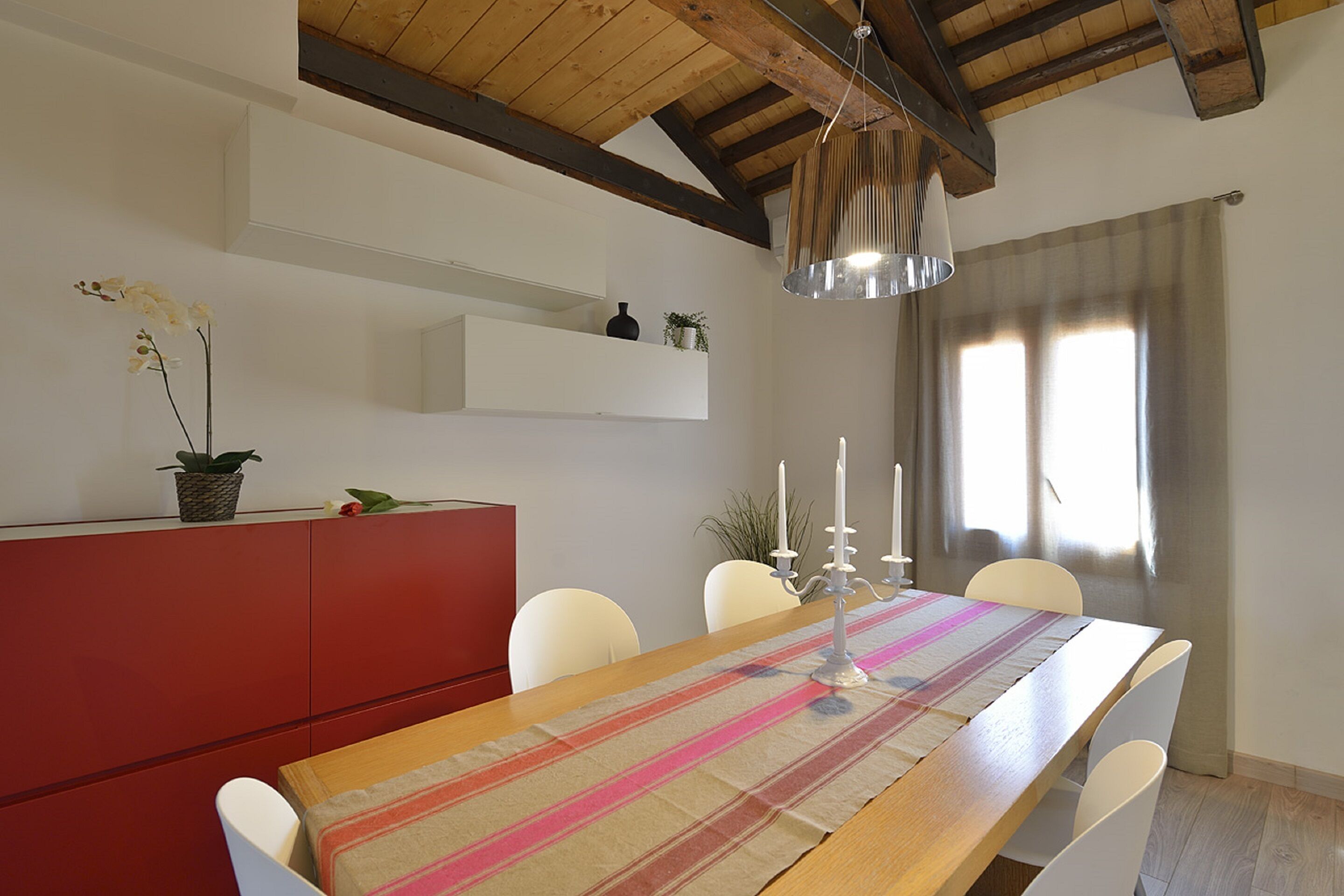 Un coin repas avec une table en bois, des chaises blanches, un buffet rouge et une suspension.