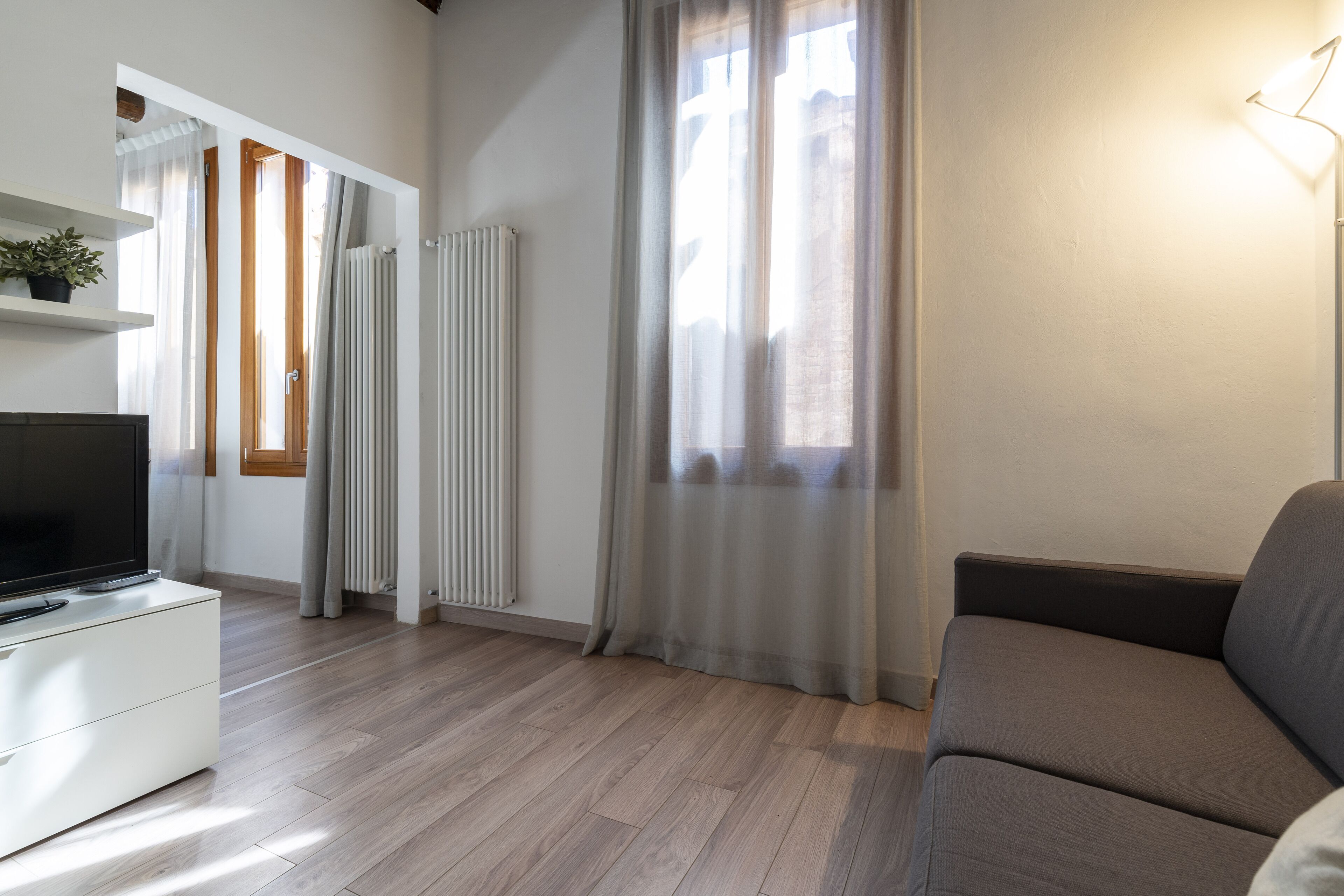 A modern living room with a flat-screen TV on a white cabinet, a grey sofa, and a wooden floor.
