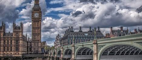 A historic bridge with arches spanning a river, connecting two sides of a city with notable buildings including a large clock tower.