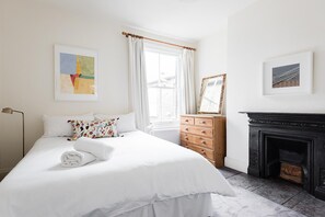A hotel room with a bed, a dresser, a fireplace, and two framed pictures on the wall. - The Battersea Apartments (London)