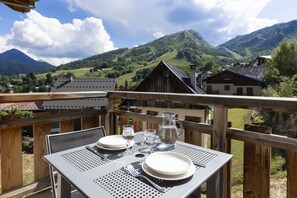 Une table dressée pour deux personnes, avec une vue imprenable sur les montagnes, une terrasse en bois et une architecture traditionnelle.