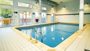 An indoor swimming pool with clear water, tiled floor, and a view of the outside through large windows.