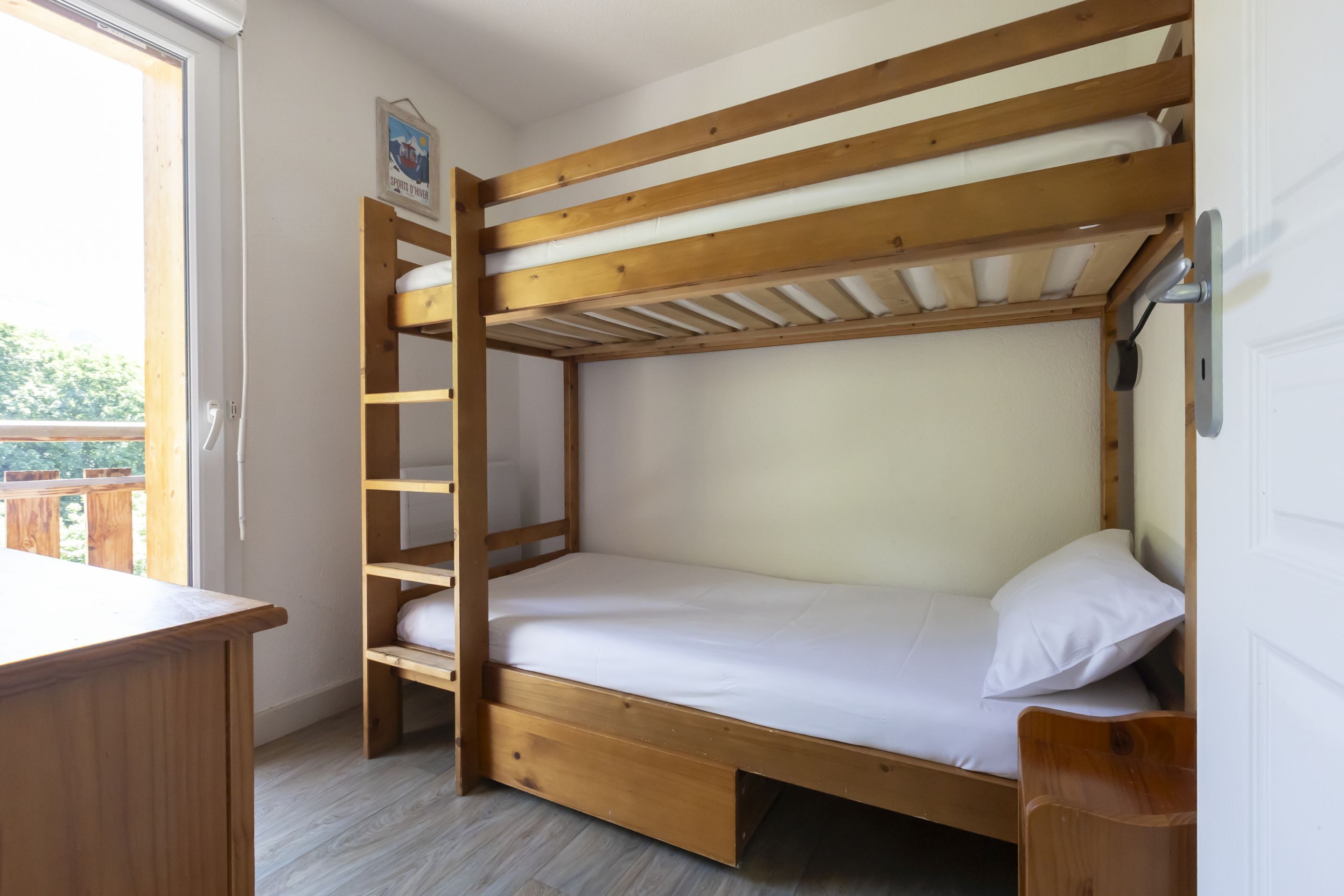 Una cama individual superpuesta con estructura de madera, un escritorio y una ventana.