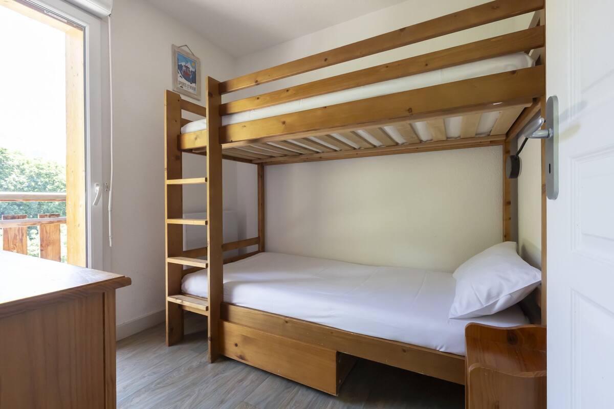 Ein Stockbett mit Holzbalken, ein Schreibtisch und ein Fenster.