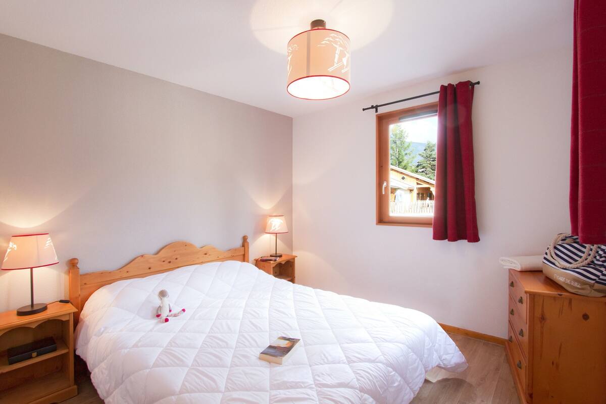 Ein Schlafzimmer mit einem hölzernen Bett, zwei Nachttischlampen, einem Nachttisch aus Holz, einer Kommode und einem Fenster mit Vorhängen.