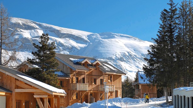 A wooden lodge with multiple balconies and a snow-covered mountain in the background. - Résidence Odalys L'Orée des Pistes (Le Dévoluy)