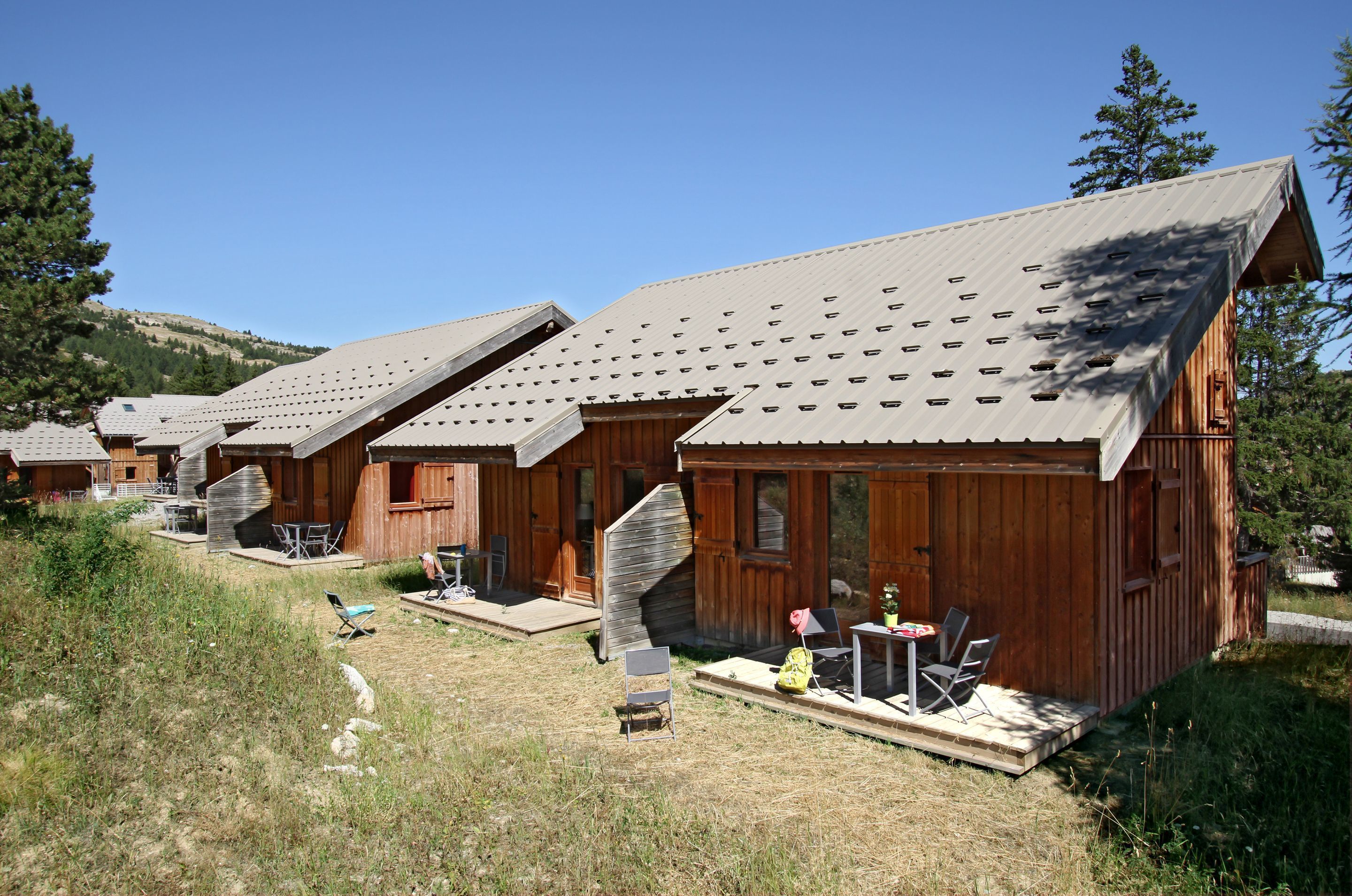 A row of wooden cabins with sloped roofs, outdoor seating, and a clear view of the surrounding landscape.