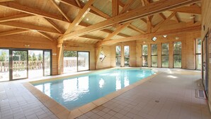 An indoor swimming pool with wooden beams, large windows, and tiled flooring. - Résidence Odalys L'Orée des Pistes (Le Dévoluy)