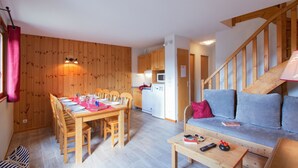 A cozy room with a wooden dining table, chairs, a sofa, and a staircase. - Résidence Odalys L'Orée des Pistes (Le Dévoluy)