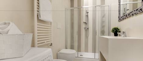 Une salle de bain moderne avec une douche à parois de verre, des toilettes blanches et un lave-linge.