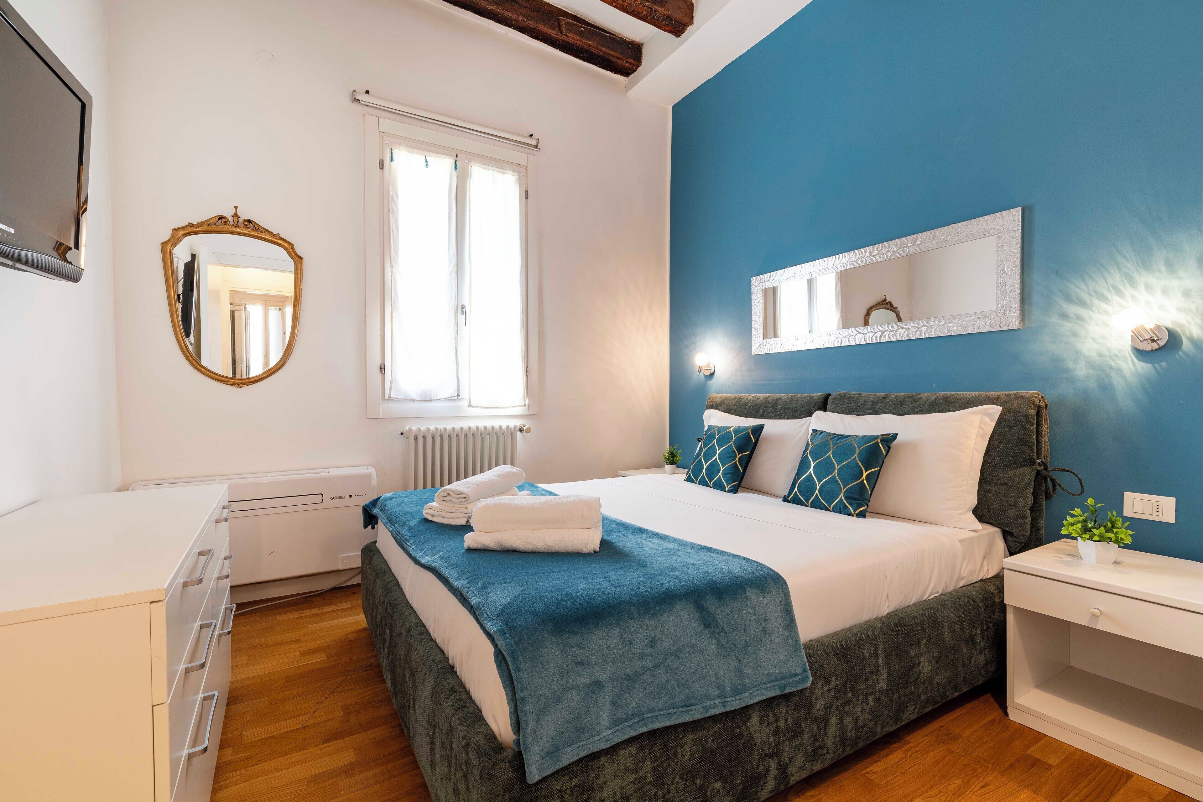 Un dormitorio con cama, mesita de noche, cómoda y una ventana con cortinas.