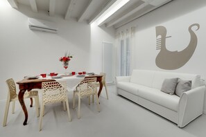 A modern living room with a white sofa, a dining table with chairs, and a wall with a decorative design. - Bacchus Venice Residence by Wonderful Italy (Venice)