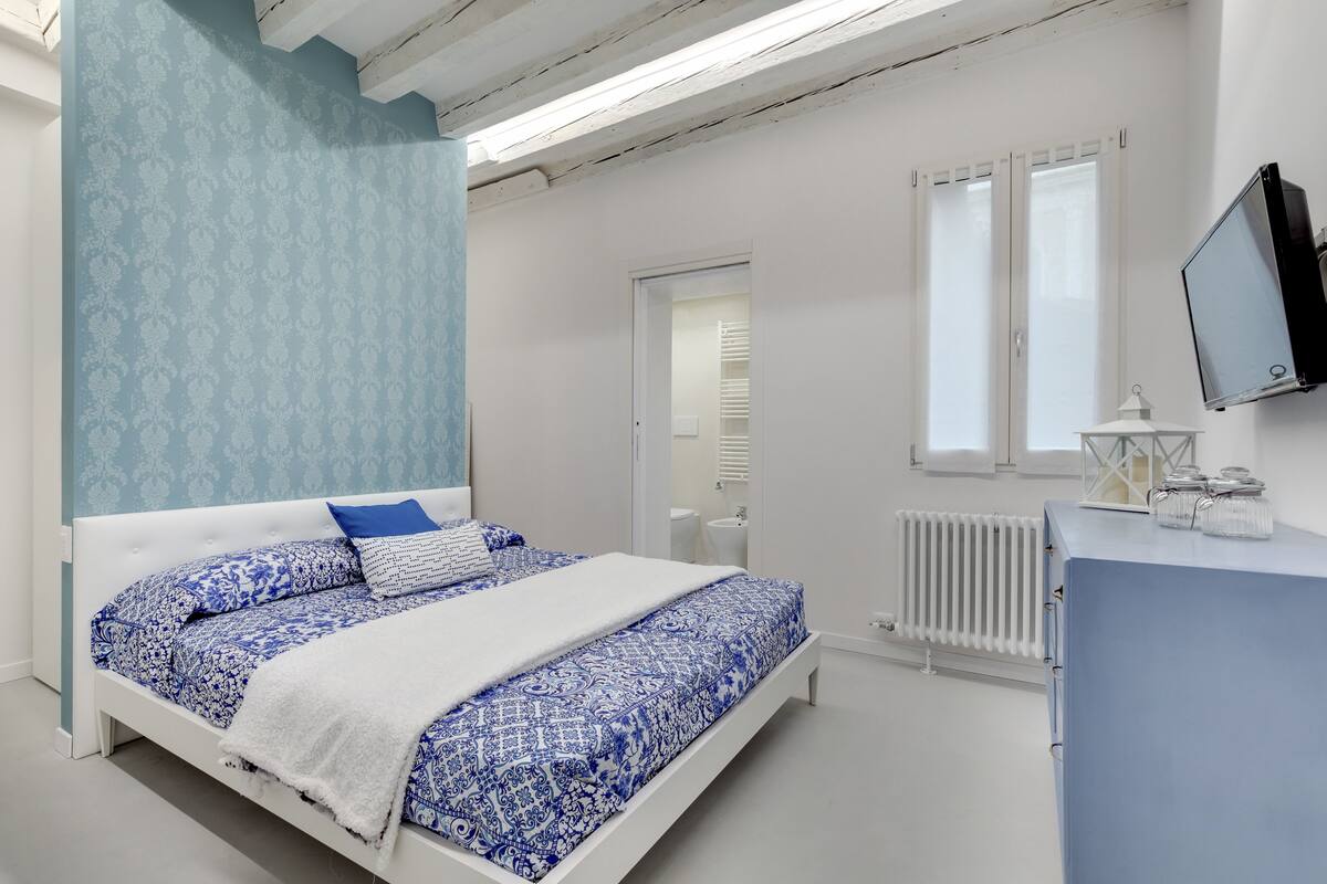A bedroom with a bed, a dresser, a TV, and a window.