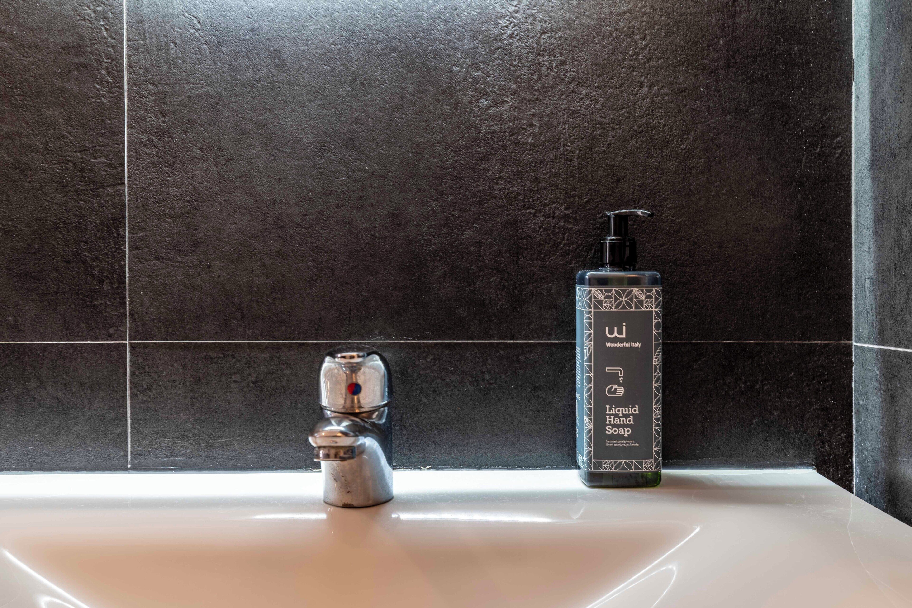 A bathroom with a modern sink, a faucet, and a bottle of liquid hand soap.