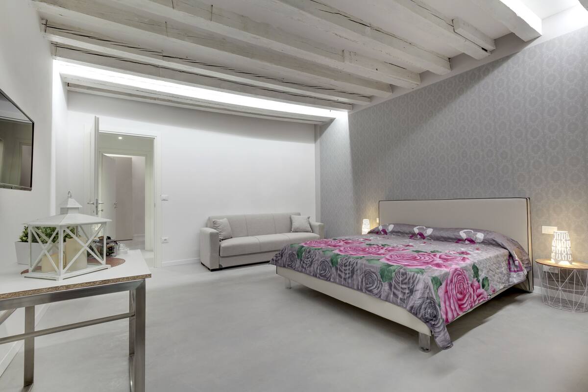 A bedroom with a bed, a sofa, a table, and a mirror.
