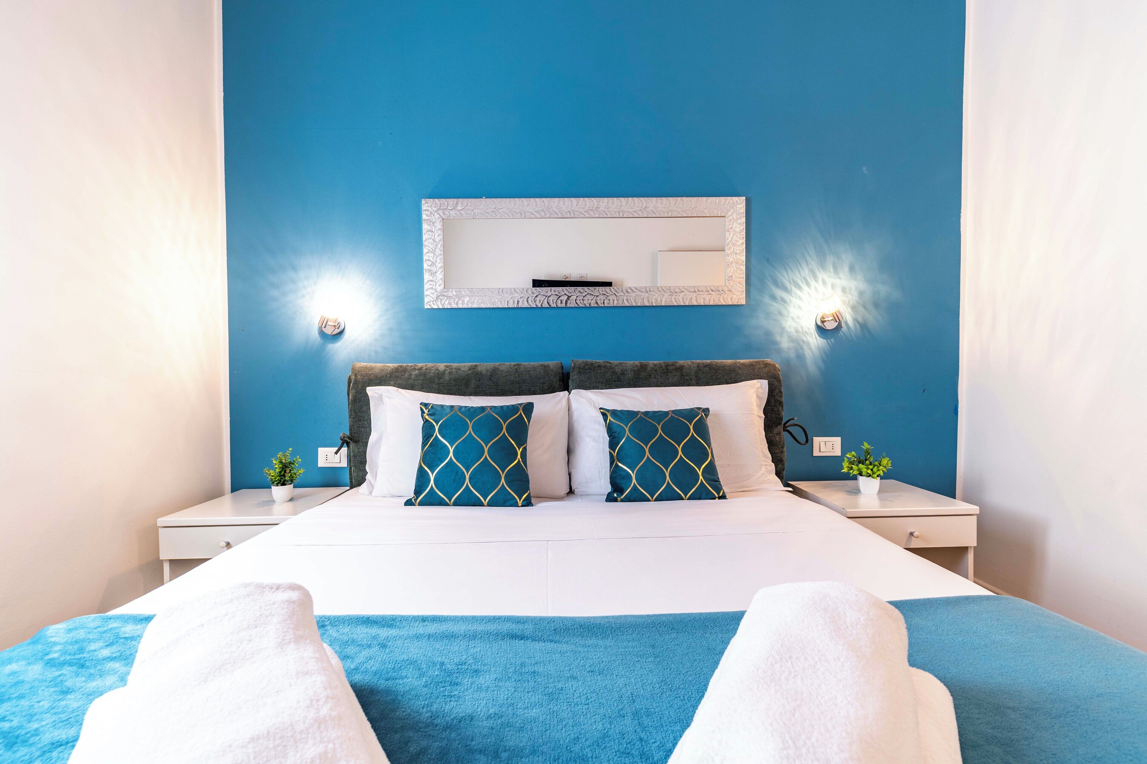 Quarto de hotel com uma cama, duas mesas de cabeceira, um espelho e uma parede azul.