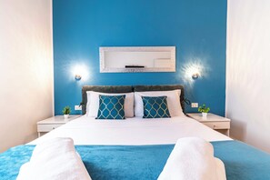Una habitación de hotel con cama, dos mesitas de noche, un espejo y una pared azul.
