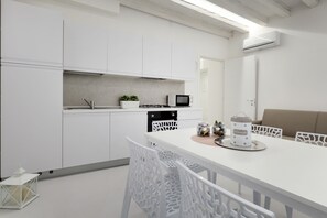 A modern kitchen with white cabinetry, a dining table with white chairs, and a microwave. - Bacchus Venice Residence by Wonderful Italy (Venice)