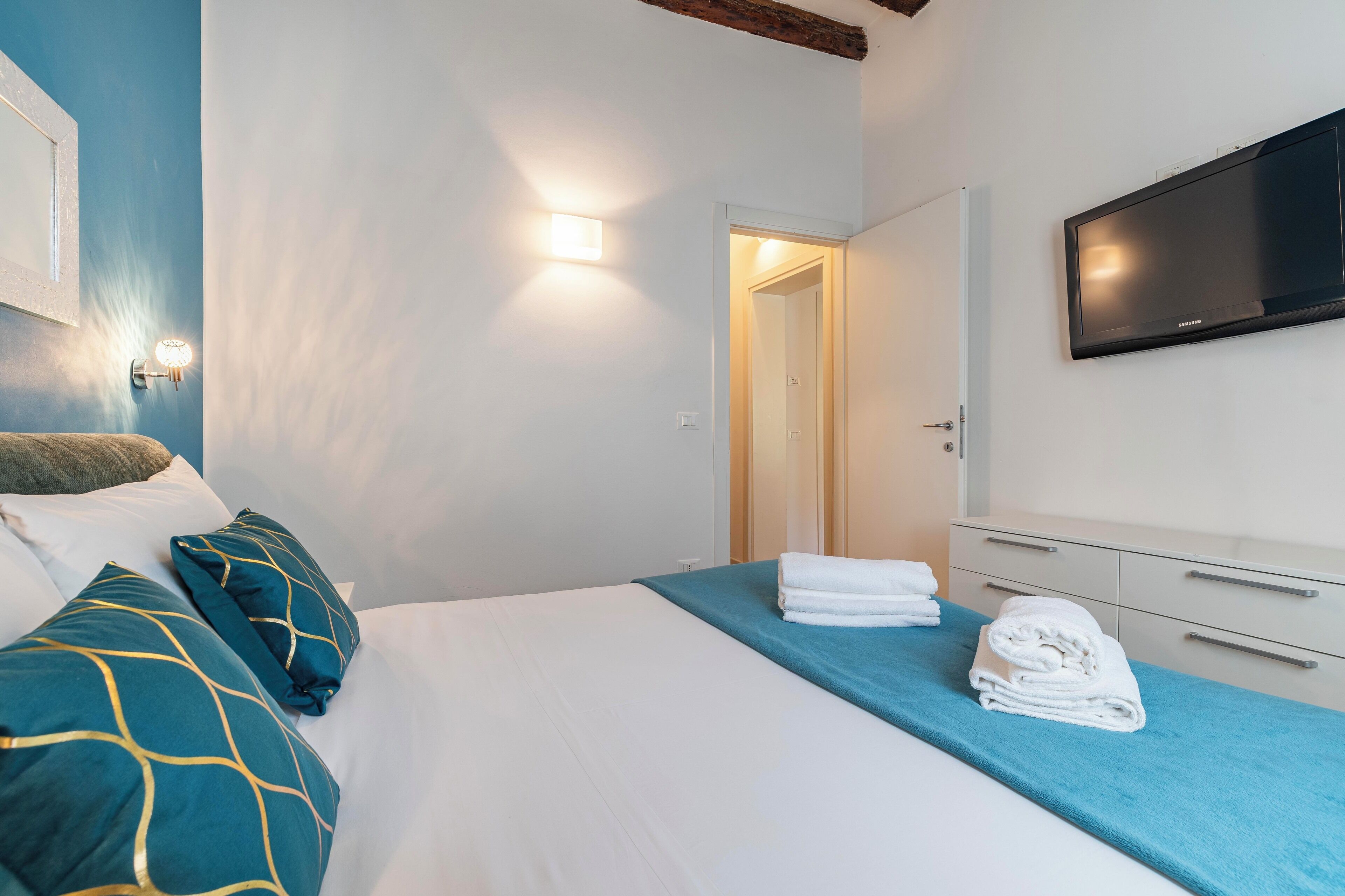 A hotel room with a bed, a TV, and a door leading to another room.
