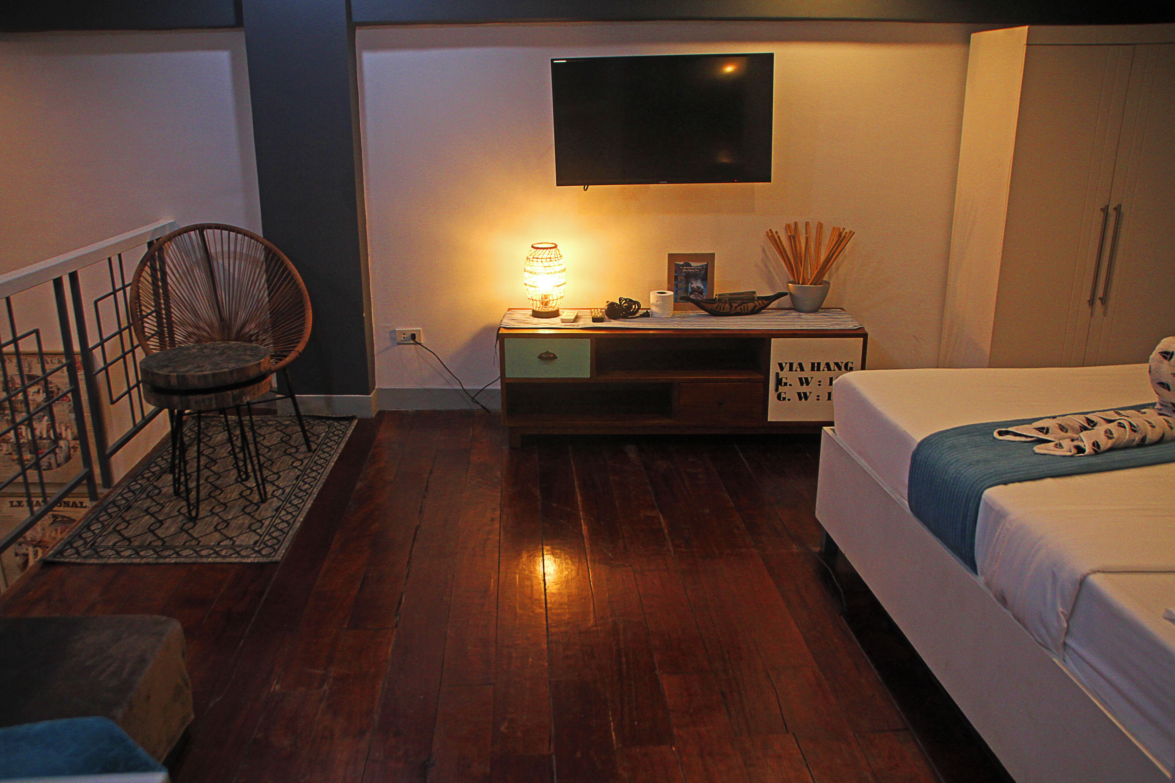 A bedroom with a bed, a TV, a chair, a nightstand, and a wooden floor.