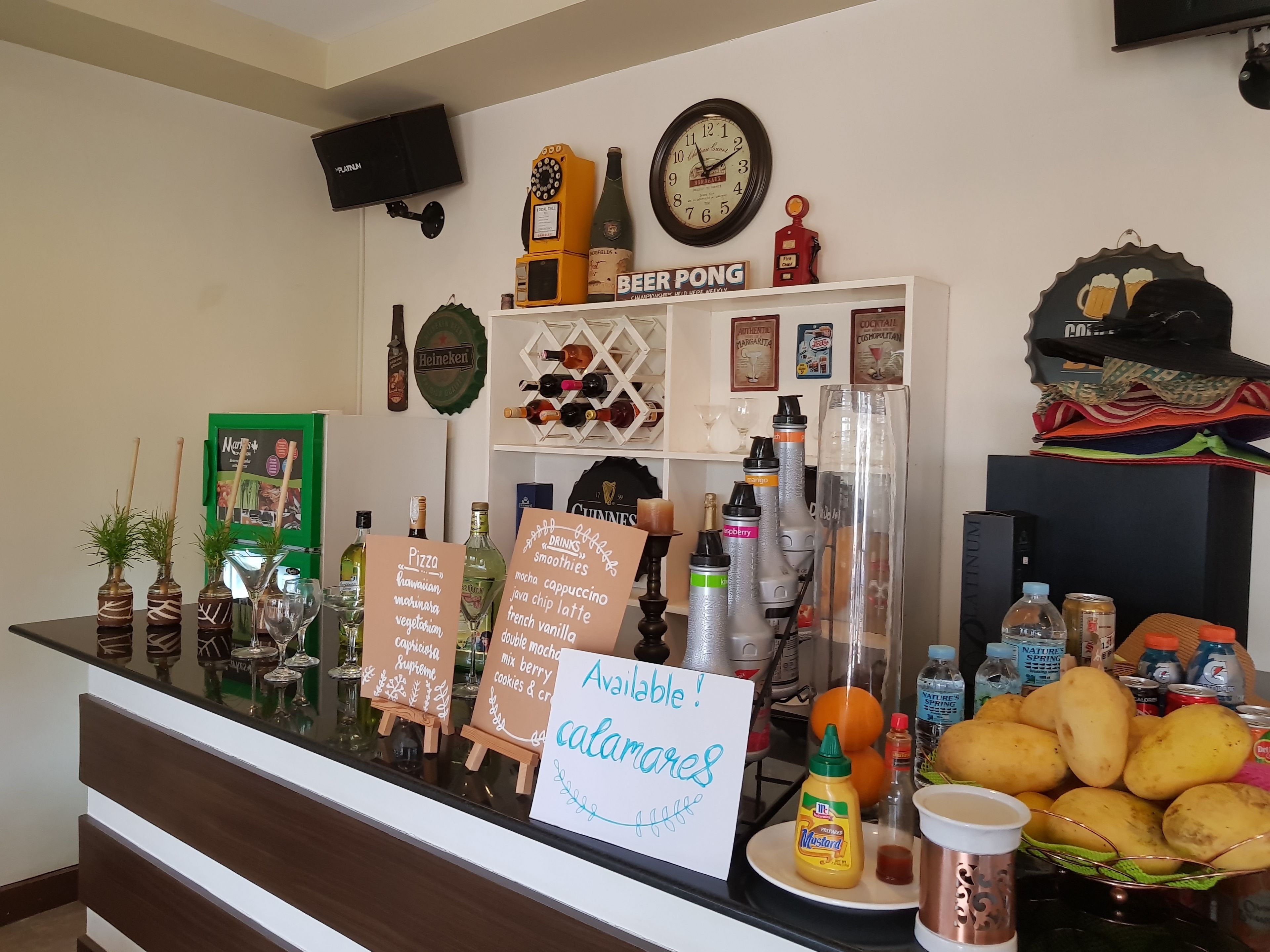 A bar area with a clock, beer pong table, and various bottles and glasses.