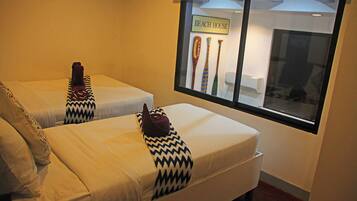 Two single beds with patterned pillows and a window with a sign reading "BEACH HOUSE".